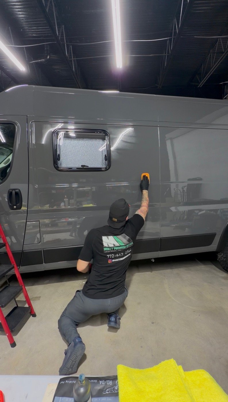 Detailer applying protection to the side of a gray camper van