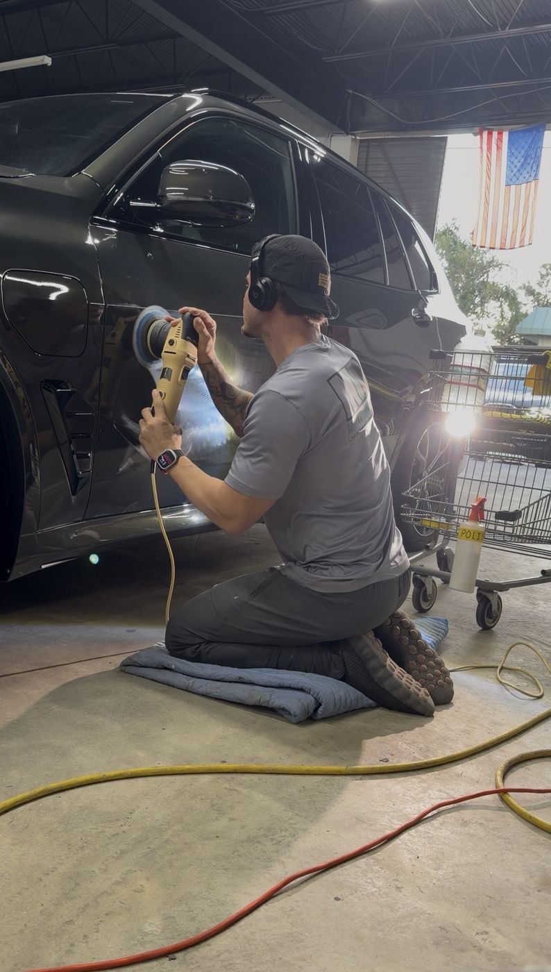 Adham machine-polishing the door of a black BMW in the shop