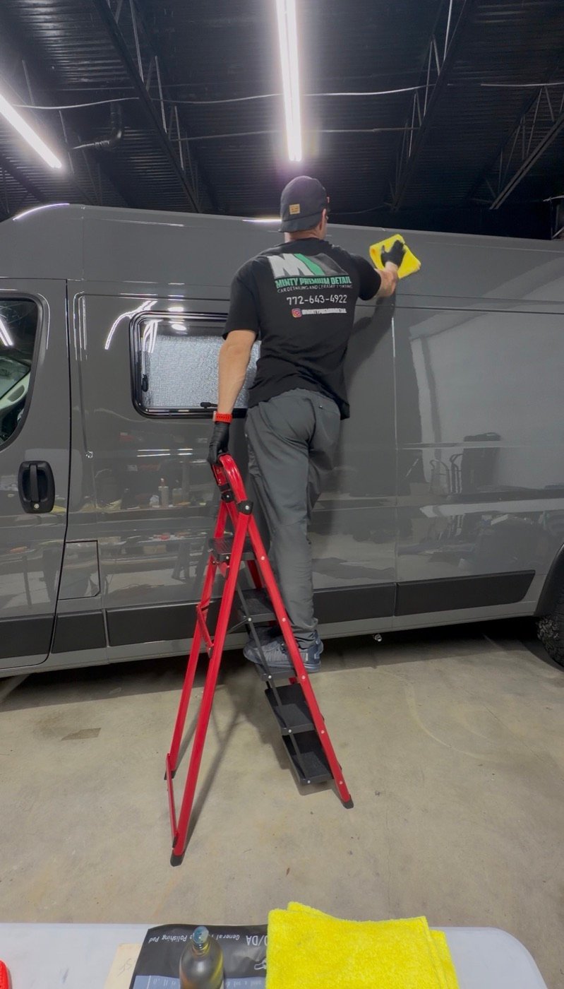 Detailer wiping the upper side of a gray van with a microfiber towel