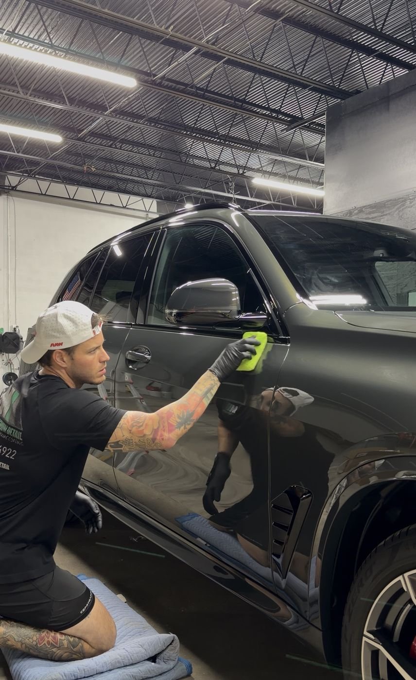 Adham applying ceramic coating to a black BMW in the Minty shop, paint reflecting like a mirror